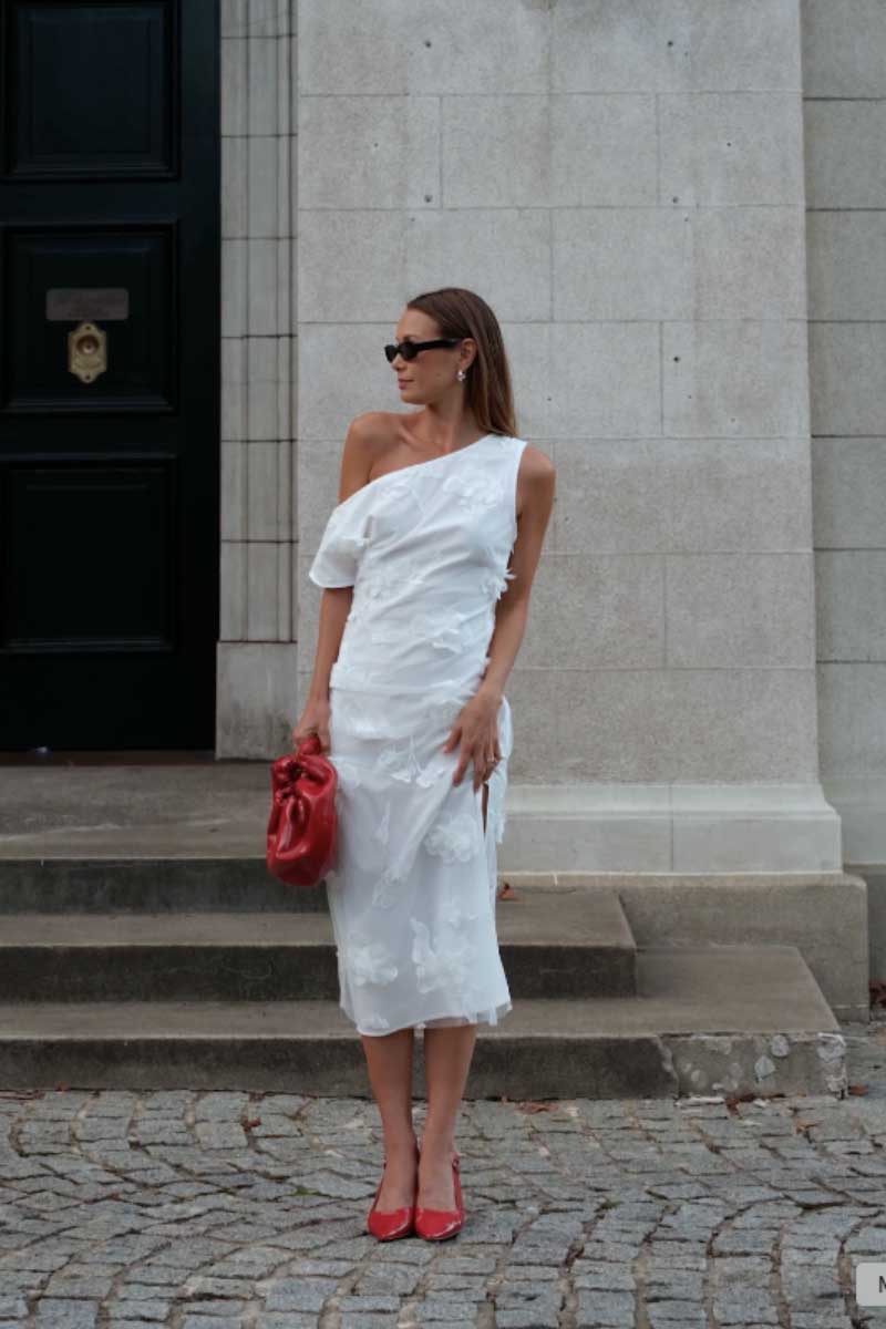 Woman in a white dress holding a red handbag on a street.