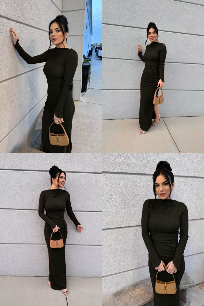 Woman in a black dress with a beige handbag posing against a light-colored wall.