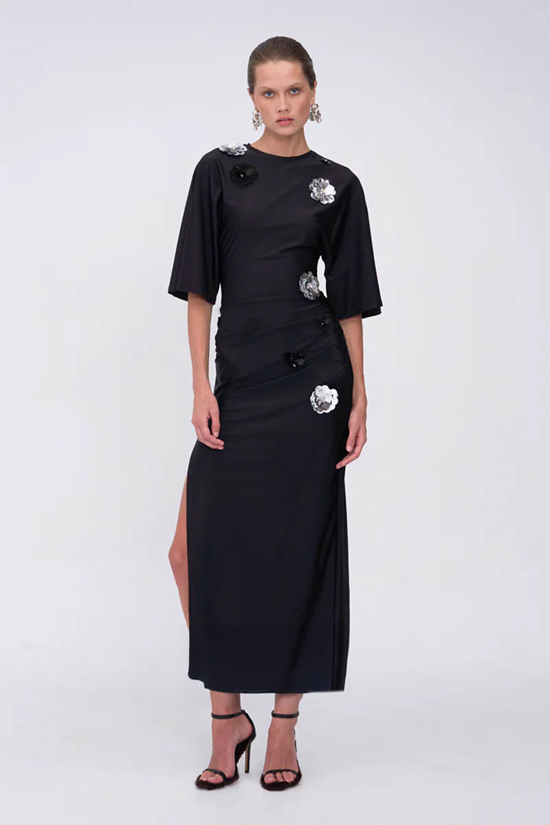 Black dress with silver buttons worn by a model on a white background