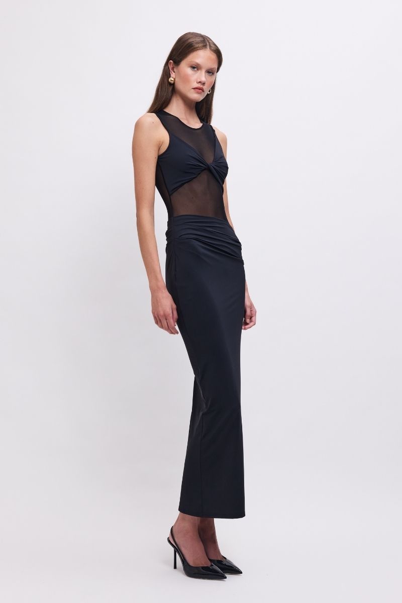 Woman wearing a black sleeveless dress with sheer panels on a white background