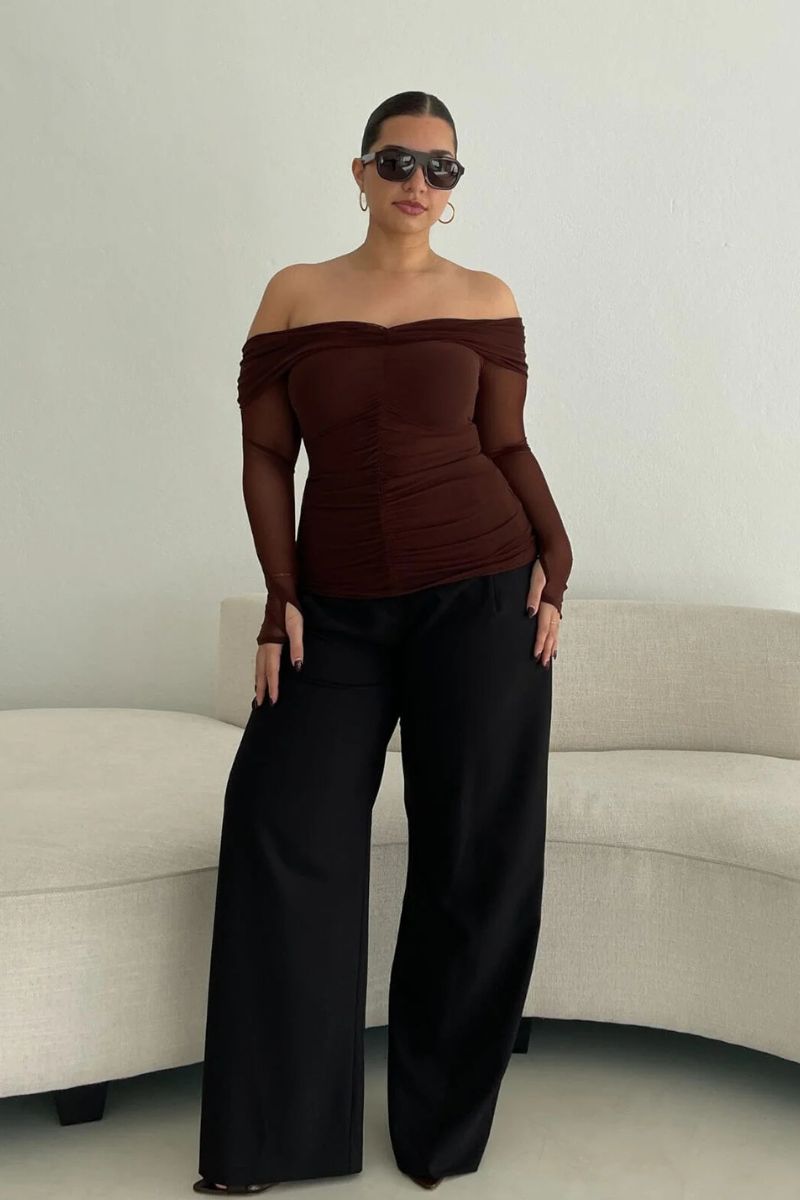Woman wearing a brown off-shoulder top and black pants.